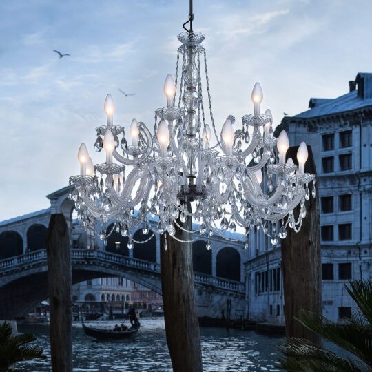 An Outdoor Crystal Glass Chandelier with glowing bulbs elegantly hangs by a historic stone building and canal bridge, while a gondola glides below and birds flutter in the cloudy sky, crafting a picturesque scene.