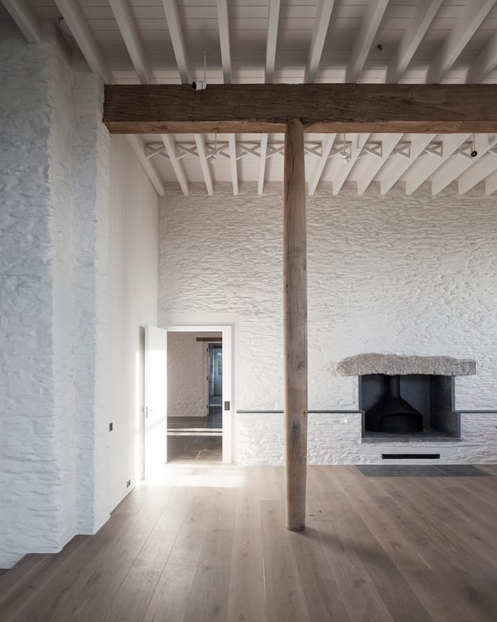 Coastal House living area with wooden floor, pillar, open fireplace, white painted stone walls RIBA Awards 2018