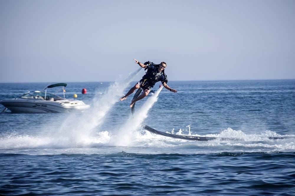 Man with Jetpack, flying above the sea, motorboat in background, yacht toys