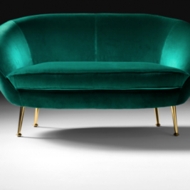 A plush, emerald green upholstered loveseat with a curved back and sleek, gold tapered legs evokes the sophistication of London. The background is gradient black to gray, creating a modern and elegant ambiance.