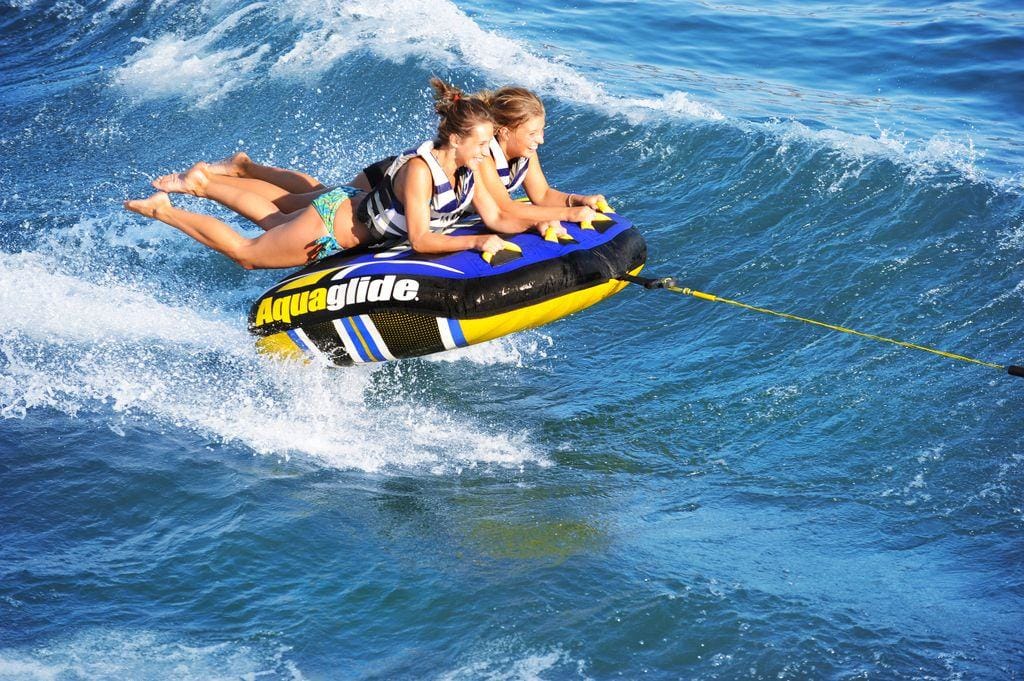 Yacht toys, inflatable cushion being towed behind a speedboat, two people hanging on