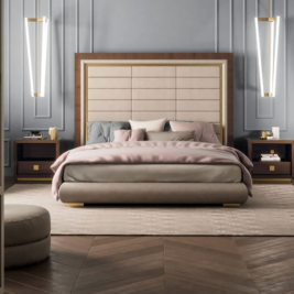 A modern bedroom featuring a large upholstered bed with pink and gray bedding, perfect for making guests feel at home. The bed is flanked by two wooden nightstands, each with a hanging pendant light. The room has a paneled, light gray wall and a herringbone-patterned wooden floor.