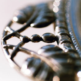 Close-up of an intricate metallic object with delicate, curved structures resembling leaves and small berries. The photo highlights the fine details and craftsmanship, with a soft-focus background.