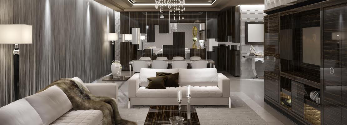 A modern and elegant living room with neutral tones features white sofas, a glass coffee table, a fur throw, tall lamps, and a bespoke dark wood media unit. In the background, a dining area with white chairs and a chandelier adds sophistication. Decor includes candles and flowers.