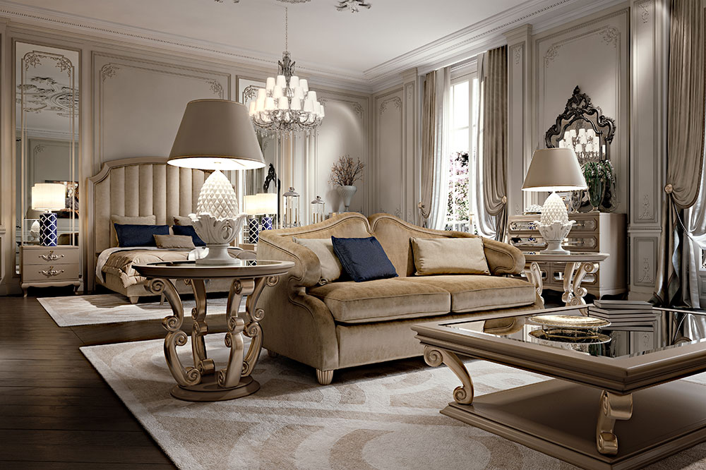 A luxurious, elegantly decorated bedroom with a beige color palette, featuring luxury Italian furniture like an upholstered bed and a plush sofa with navy blue pillows. Ornate side tables with lamps, a large mirror, and a chandelier. Rich drapes and intricate moldings complete the sophisticated look.