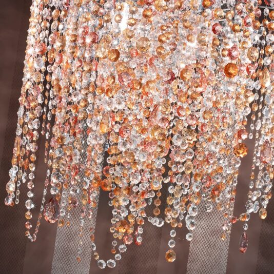 Multi Coloured Round Italian Chandelier The Multi Coloured Round Italian Chandelier exudes luxury as it hangs from the ceiling, adorned with cascading crystals in amber and clear hues. The intricate design features numerous sparkling beads and dangling ornaments, creating a shimmering effect against a dark background.