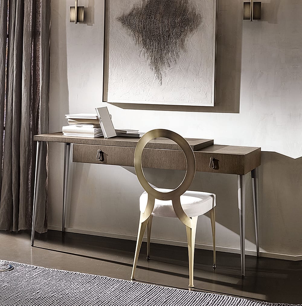 A sleek, modern home office features a wooden desk with two drawers and metal legs. An open laptop and a few books rest on the desk. A distinctive chair with a circular back and cushioned seat is positioned in front. Above the desk hangs a large abstract art piece, perfect for working from home.
