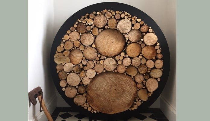 A decorative wooden log storage display features various sizes of cut logs arranged in concentric circles within a black circular frame. Positioned on the balcony, a metal axe leans against the wall to the left, while the floor boasts a black-and-white checkered tile pattern.