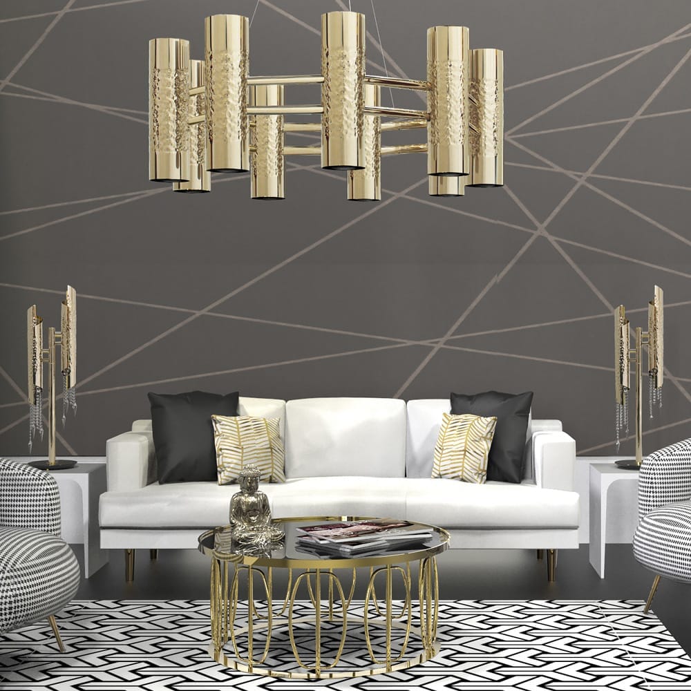 A modern living room with a white sofa adorned with black and white patterned cushions. Above the sofa hangs a gold cylindrical chandelier, enhancing the lighting in the room. A round glass coffee table with a gold base sits on a black and white geometric rug. The walls are decorated with a geometric pattern.