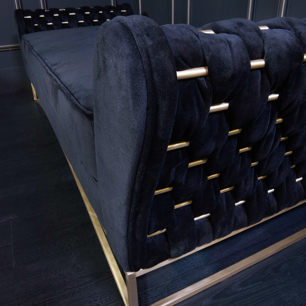 A close-up view of a luxurious dark blue or black velvet couch, part of an exclusive luxury furniture collection, features a woven backrest design with gold accents. Set against a modern, dark-colored interior background, the sleek and elegant piece emphasizes intricate craftsmanship and style.