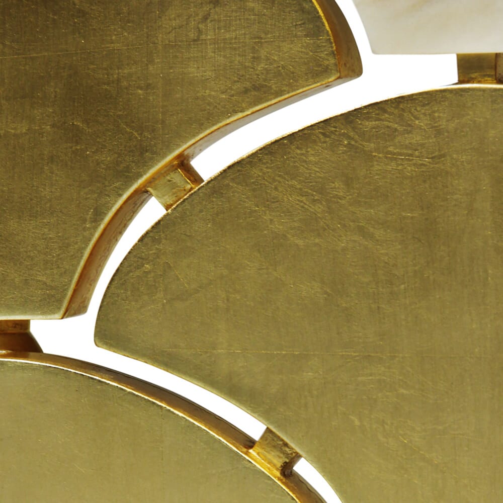 Close-up image of overlapping, fan-shaped pieces with a reflective gold finish. The pattern appears to be decorative, with visible seams and a smooth, polished texture. The sections create a geometric and artistic effect, reminiscent of a luxury furniture collection.