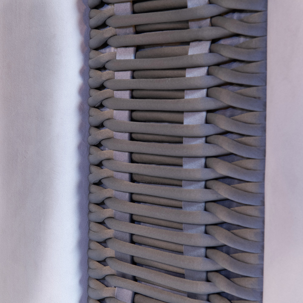 A close-up of a woven textile with a repetitive, intertwined pattern. The fabric is composed of tightly interlocked threads, creating a textured, three-dimensional appearance. The colors are muted, with shades of gray and light purple, perfect for adding sophistication to any luxury furniture collection.