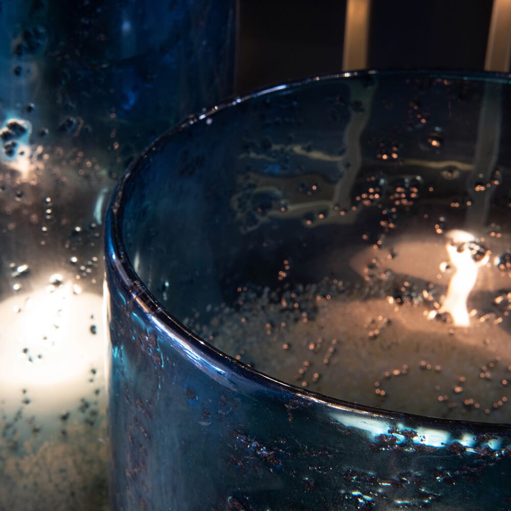 Close-up of two translucent dark blue glass vessels illuminated from inside, highlighting their textured surface with numerous small bubbles. The ambient lighting creates a warm and tranquil atmosphere, reminiscent of a luxury furniture collection's exquisite details.