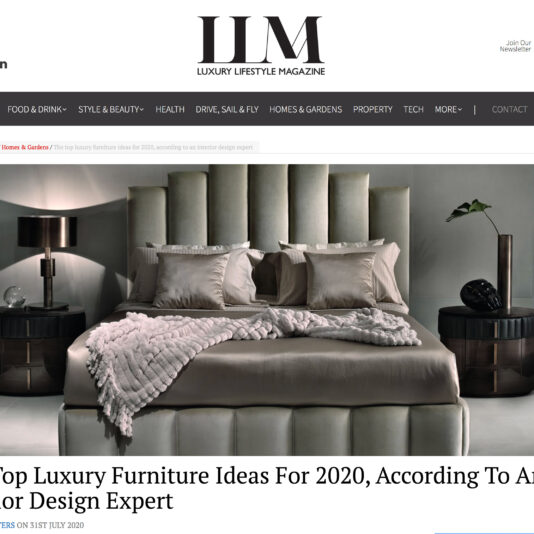 A webpage from "Luxury Lifestyle Magazine" featuring an article titled "The Top Luxury Furniture Ideas For 2020, According To An Interior Design Expert." The image shows a stylish bedroom with a plush bed, modern decor, a lamp, and a plant.