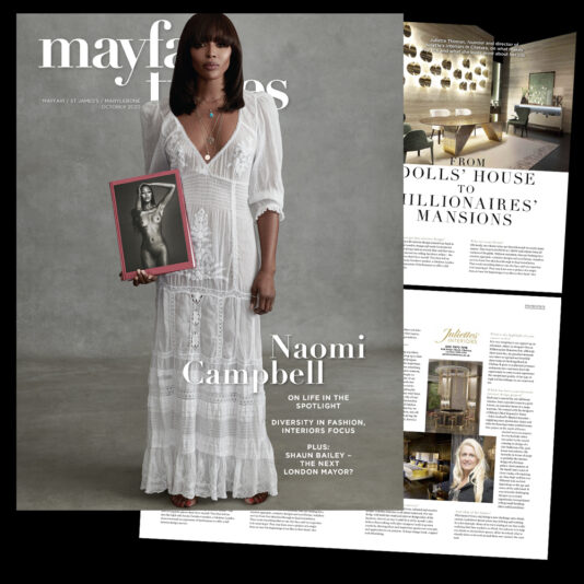 A magazine cover featuring a woman in a white dress holding a picture of another person. The text on the cover reads "Mayfair Times," along with the name "Naomi Campbell" and other article titles. Two interior pages with articles and images are also visible.