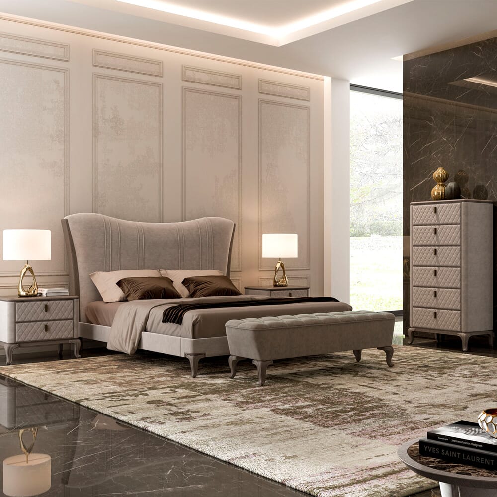 A modern, luxurious bedroom interior design features a large upholstered bed with brown bedding and a matching bench. It includes two bedside tables with lamps, a tall dresser, and a large window letting in natural light. The walls are paneled, and the floor is covered with a patterned rug.