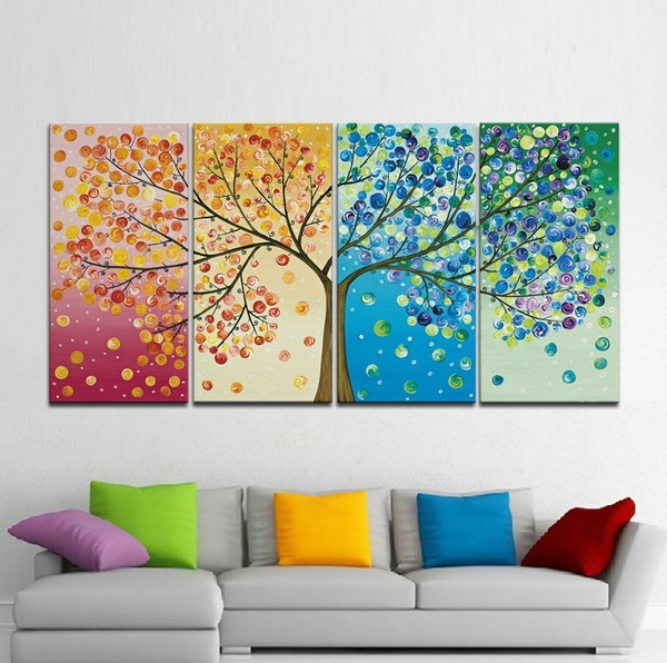 Four-panel artwork depicting a tree in different seasons hangs above a modern grey couch with colorful cushions. Each panel shows the tree in various colors: pink and orange for spring, yellow for summer, blue for autumn, and green for winter—a perfect way to style your home office.