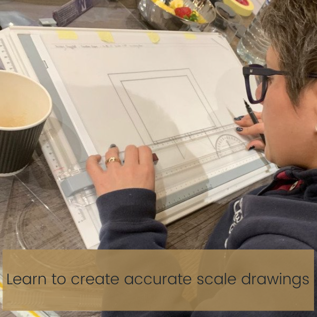 A person wearing glasses and a dark sweatshirt uses a pencil and ruler to create a detailed drawing on a large sheet of paper. A paper cup and drafting supplies are on the table. Text overlay reads, "Learn to create accurate scale drawings in our online interior design course.