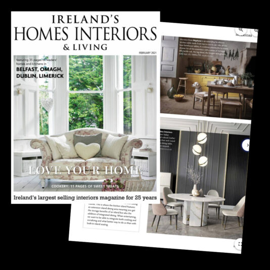 An open magazine titled "Ireland's Homes Interiors & Living." The cover features a cozy couch with a heart-shaped pillow in a bright living room. Inside pages showcase modern dining and living room furniture with elegant decor, emphasizing contemporary interior design.