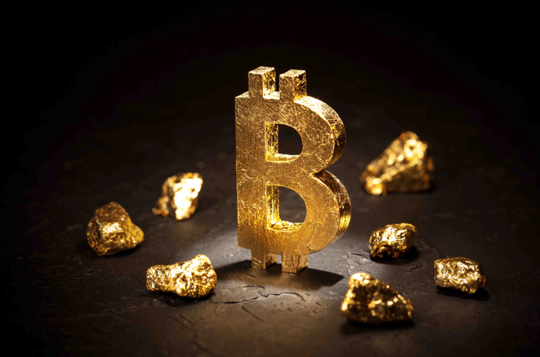 A large, gold Bitcoin symbol stands upright on a dark surface, surrounded by several gold nuggets. The image is well-lit, highlighting the shiny texture of the symbol and nuggets against the dark background, suggesting a sharp increase in crypto transactions by luxury spenders.