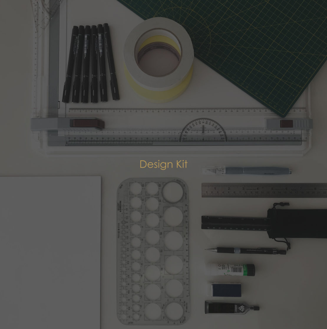 A design kit is laid out on a table, including drafting tools such as a drawing board, a cutting mat, tape, pens, rulers, a circle template, and glue. The words "Design Kit" appear in the center of the image. Become your own Interior Designer with these essential tools at your fingertips.