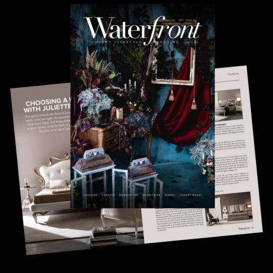 A dark floral-themed magazine cover titled "Waterfront" is overlaid on two other open magazine pages. The cover features a luxurious interior setting with deep red curtains, ornate candles, and floral arrangements, exuding an opulent atmosphere.