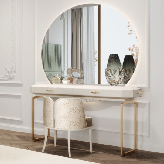 A modern vanity setup featuring a large, round, lighted mirror above a white and gold desk with decorative items such as a lace-patterned container, perfume bottles, and two vases. This art deco interior design includes two upholstered chairs with a subtle pattern placed under the desk.