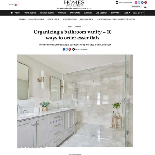 A Homes & Gardens web page titled, "Organising a bathroom vanity – 10 ways to order essentials," features a modern bathroom with a double sink vanity, white cabinets, a large mirror, and a glass shower. The space is bright and minimalistic with a clean, organized aesthetic.