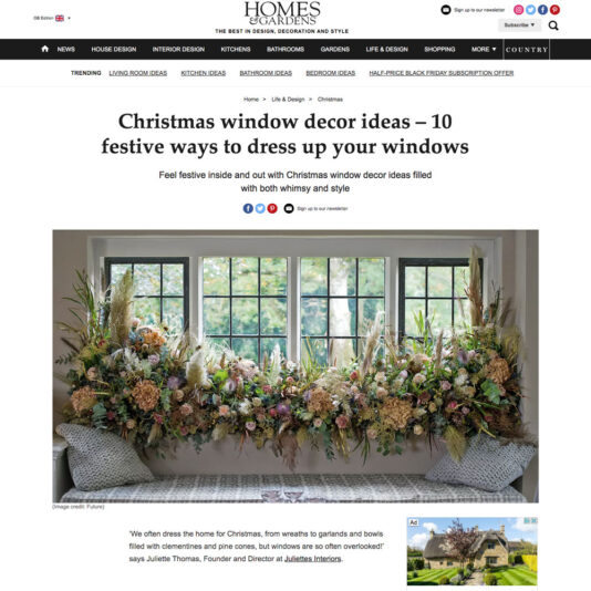 A webpage from Homes & Gardens featuring a headline about Christmas window decor ideas. Below the headline, there is an image of an elaborate window display with various festive flowers and greenery. The menu bar and website logo are visible at the top.