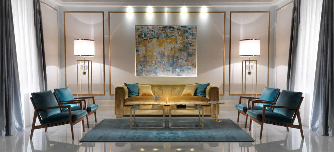 A modern living room with a mustard-yellow sofa, two teal armchairs, a glass coffee table, and a blue rug. The walls are adorned with a large abstract painting and flanked by two standing lamps. For luxury living room ideas, the space is harmoniously framed with white curtains and gold accents.