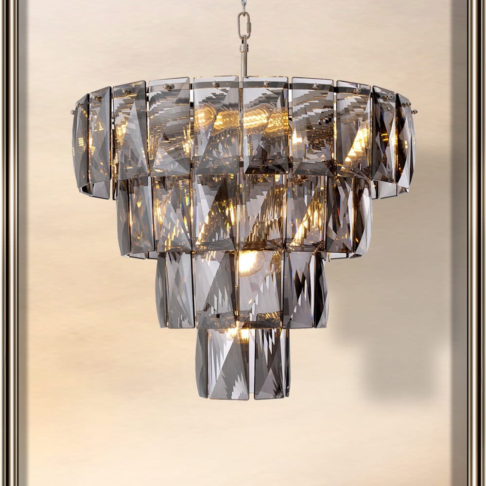 A luxurious chandelier with multiple tiers of rectangular, faceted crystal pieces, emitting a warm, glowing light. The crystals are arranged in a cascading pattern, evoking the elegance of art deco interior design against a neutral background.