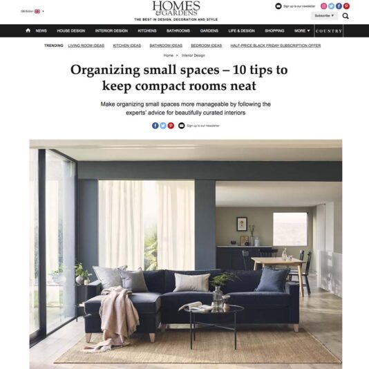 A 'Homes & Gardens' magazine webpage featuring the article "Organizing small spaces – 10 tips to keep compact rooms neat." The image showcases a modern living room with a blue sofa, coffee table, and decor illuminated by natural light.