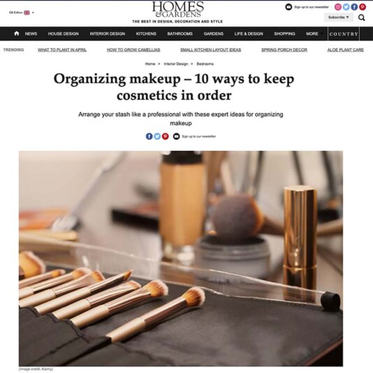 A screenshot of a Homes & Gardens article titled "Organizing makeup – 10 ways to keep cosmetics in order." The image shows an assortment of makeup brushes and cosmetics neatly arranged on a black organizer. The background is slightly blurred, highlighting the precision and elegance promoted by Homes & Gardens.