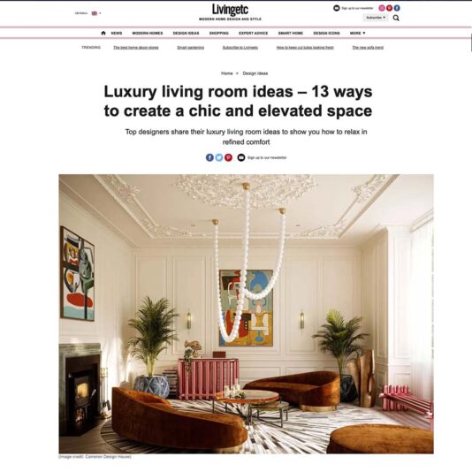 A luxurious living room with ornate white ceilings and a neutral color palette. The room features brown velvet sofas, a circular gold-trimmed coffee table, and contemporary artwork on the walls. A large chandelier hangs from the ceiling, adding an elegant touch.