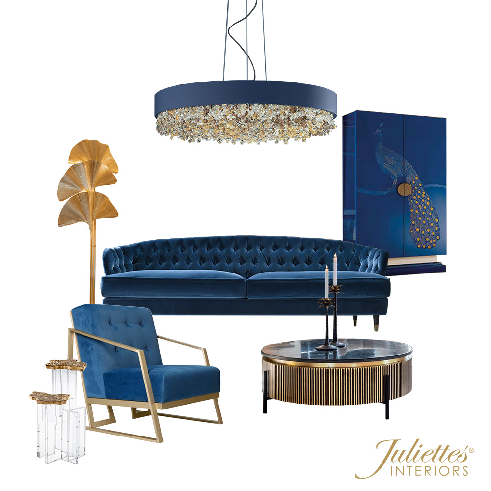 A luxurious living room setup reminiscent of the grandest rooms of Queen Elizabeth, featuring a blue velvet tufted sofa, matching blue velvet armchair with gold accents, round coffee table with fluted base, gold leaf floor lamp, blue peacock artwork, and a crystal-detailed chandelier. Branding: Juliette's Interiors.