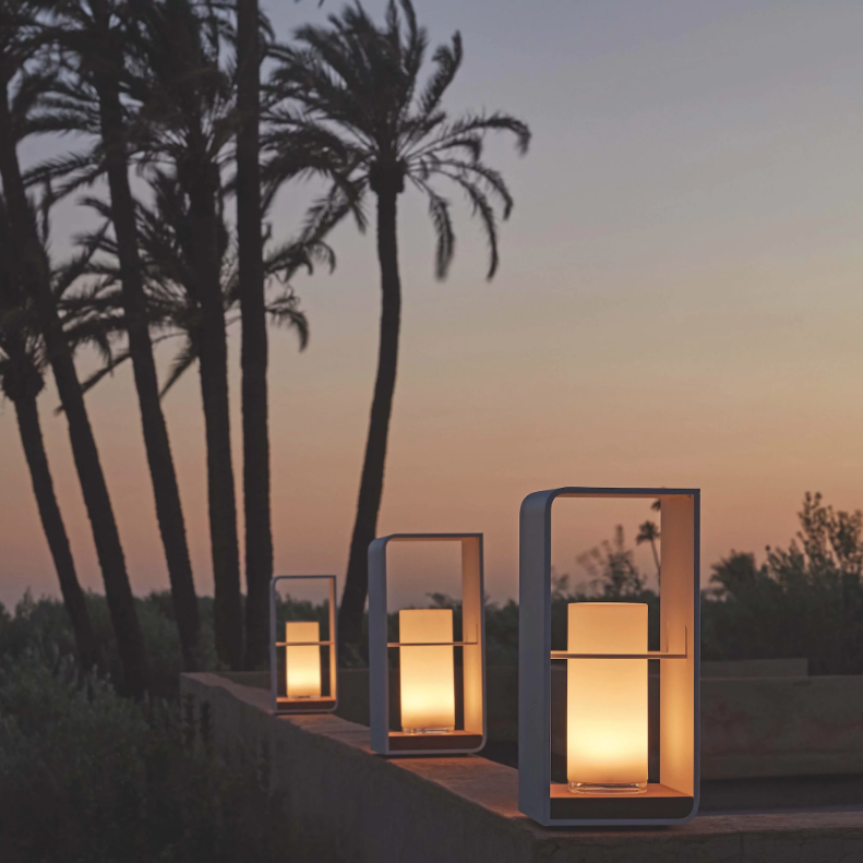 Outdoor lanterns softly illuminated on a stone ledge at dusk, with tall palm trees silhouetted against a gradient sky transitioning from deep blue to soft orange, creating the perfect ambiance for a Wimbledon-style lawn party.