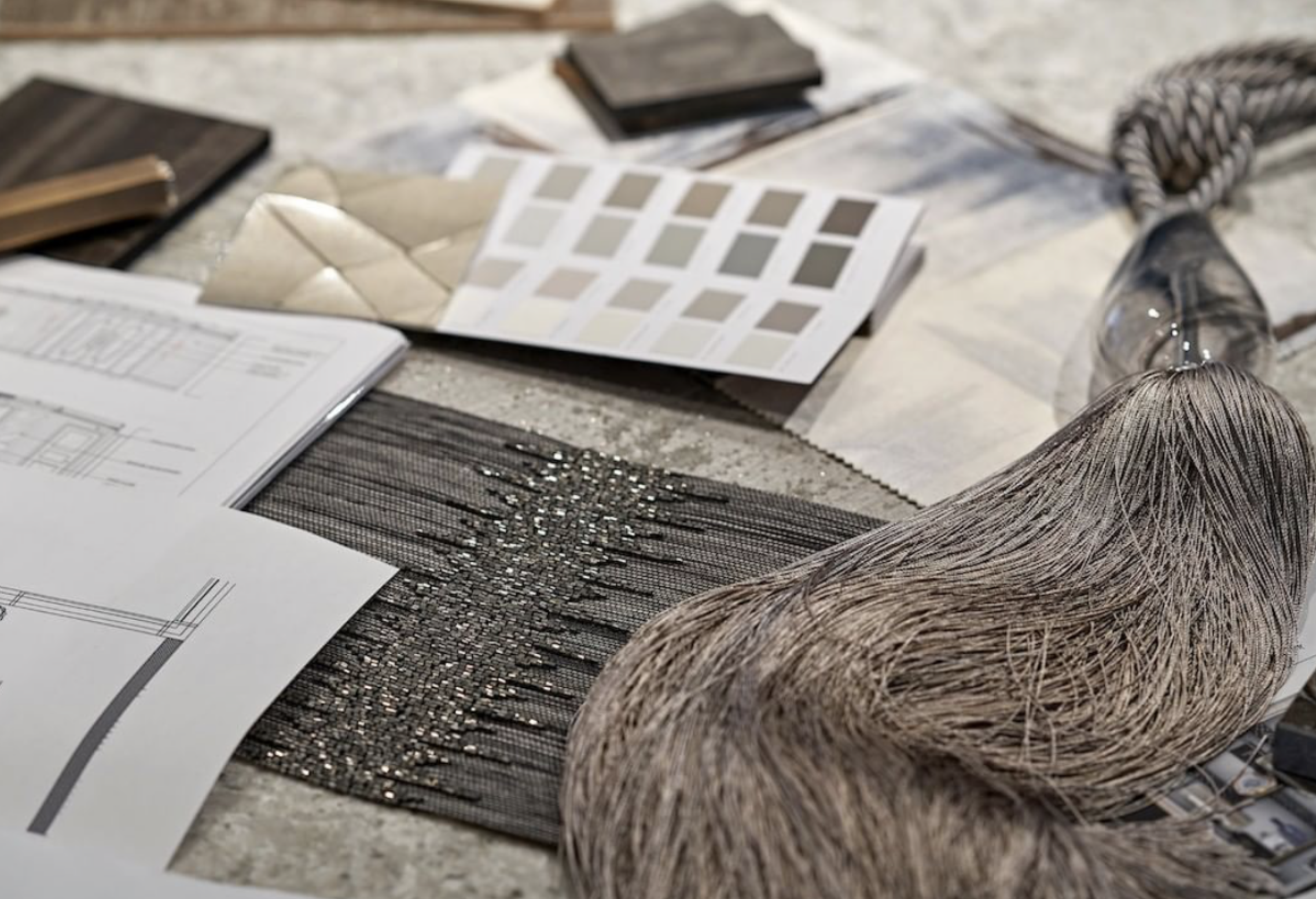 A tabletop covered with various interior design materials, including fabric swatches, color samples, design blueprints, and textured samples. The items appear to be arranged for a design presentation or project planning session for an Interior Design Course.