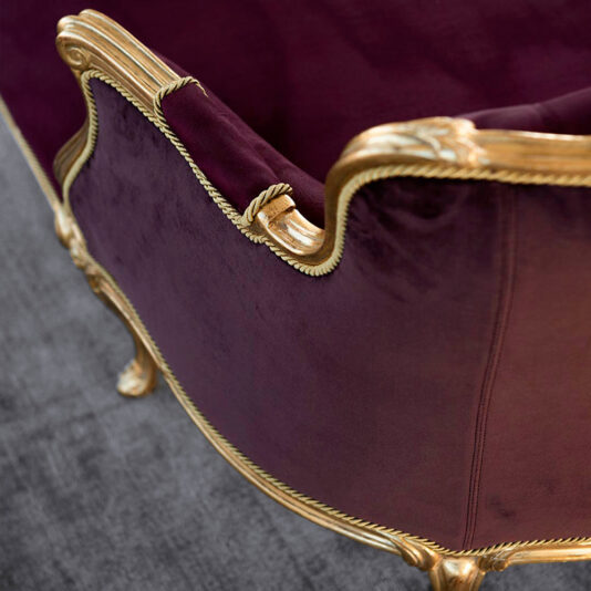 Classic Louis XVI Style Chaise Longue Close-up view of the Classic Louis XVI Style Chaise Longue, elegantly upholstered in rich purple velvet with intricate gold detailing on the edges. The armchair is positioned on a gray textured floor, exuding an opulent and luxurious ambiance.