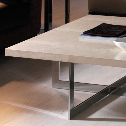 Contemporary Wooden Coffee Table A modern living room with a Contemporary Wooden Coffee Table featuring a sleek metal frame. On the table, there are a few books stacked and a white bowl. The floor has a light wood finish and part of a brown sofa is visible in the background.
