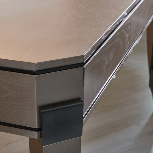 Contemporary Wooden Writing Desk A close-up of the corner of the Contemporary Wooden Writing Desk reveals its sleek, modern design with a slightly textured, metallic surface. The desk showcases clean lines and a minimalist aesthetic, supported by dark rectangular legs that enhance its overall contemporary appeal.