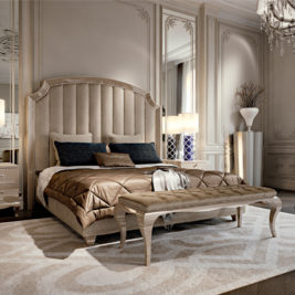 Luxurious bedroom with a large upholstered bed adorned with pillows and a plush blanket. The room showcases how to design a boutique hotel-style bedroom, featuring elegant wall paneling, a stylish bench at the foot of the bed, and ornate decor including a floor lamp, vase on the nightstand, and chandelier.