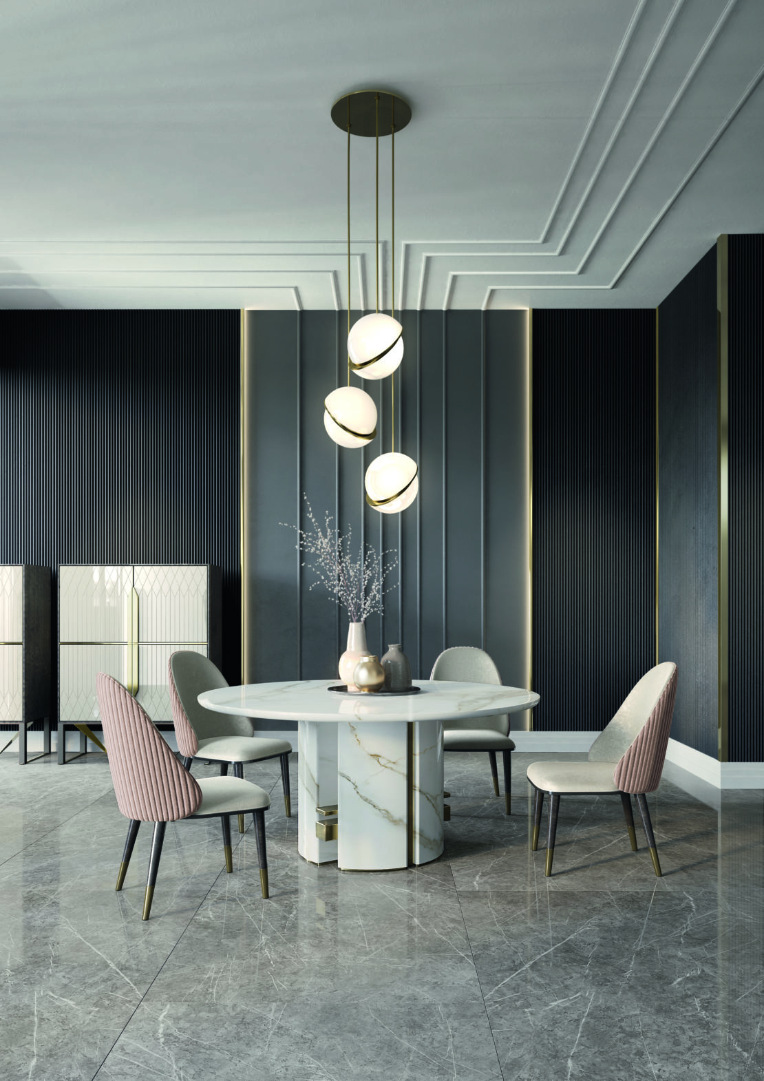 A modern dining room featuring a round marble table with a vase of branches as a centerpiece, surrounded by four chairs – two pink and two white. Above the table are three spherical pendant lights in a vertical arrangement. The floor is a glossy gray marble.