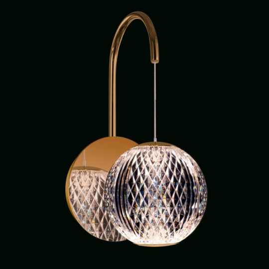 A modern wall-mounted light fixture with a gold arched arm. It features a spherical, intricately patterned crystal lampshade that emits a warm, inviting light. This example of affordable luxury lighting is both elegant and sophisticated, suitable for contemporary decor.