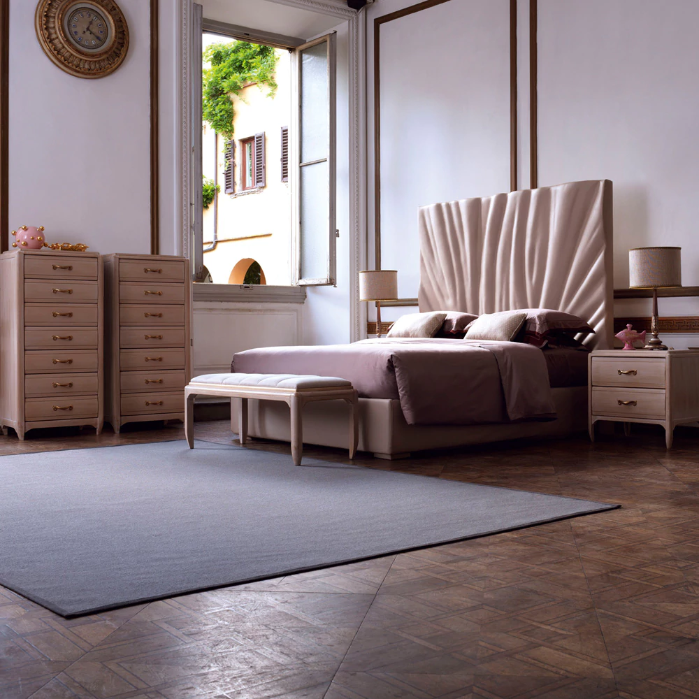 Elegant bedroom with a large, tufted headboard and neutral bedding. The room features tall dressers with storage, a bench at the foot of the bed, and two bedside tables with lamps. A large window allows natural light to brighten the space, perfectly complementing chosen home colour schemes.