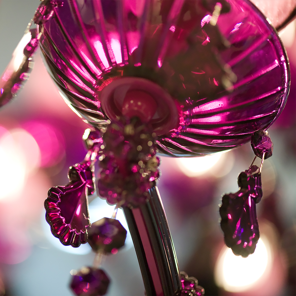 Close-up of a chandelier with dazzling, purple glass ornaments and hints of viva magenta. The central piece is surrounded by hanging faceted crystals that catch the light, creating a vibrant and luminous effect.