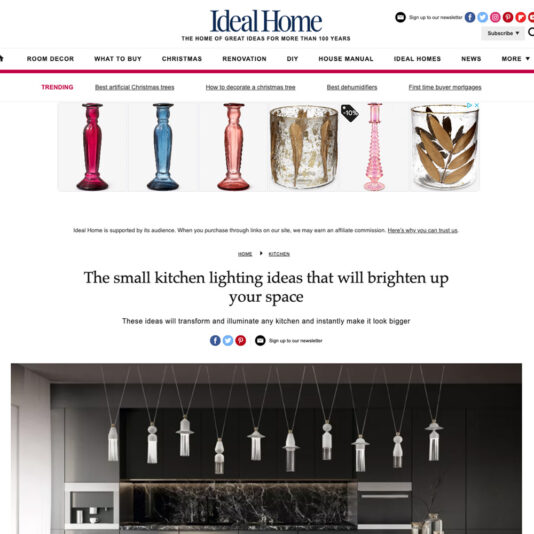 A screenshot of the Ideal Home website. The article is titled "The small kitchen lighting ideas that will brighten up your space." The page showcases nine modern pendant lights hanging above a minimalist kitchen island. The website’s navigation bar and trending articles are also visible at the top.