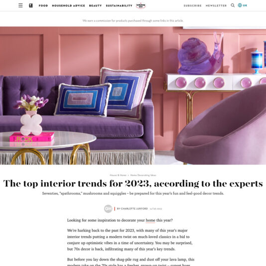 A magazine page featuring "The top interior trends for 2023, according to the experts." The page showcases a vibrant living room with a purple sofa, pink walls, and eclectic decor. The article explores hot interior trends for 2023, including seventies style, mushrooms, and squiggles.