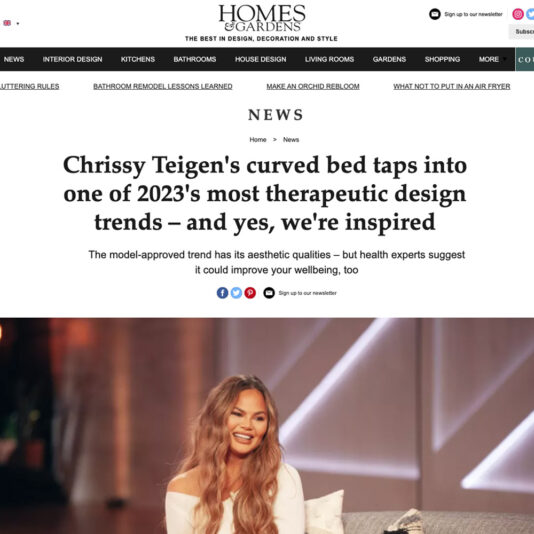 Screenshot of Homes & Gardens website article about Chrissy Teigen's curved bed being one of 2023's therapeutic design trends. The article praises the curved furniture trend for its aesthetic and potential wellbeing benefits. Chrissy Teigen is seated and smiling on a set.