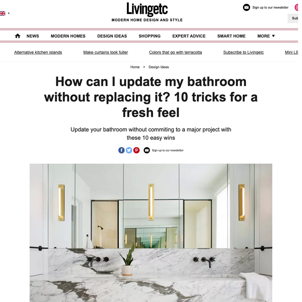 A webpage from "Livingetc" featuring an article titled "Update Your Bathroom Without Replacing It: 10 Tricks for a Fresh Feel." The page includes a header, navigation links, and an image of a modern bathroom with a double sink, marble countertop, and stylish lighting fixtures.