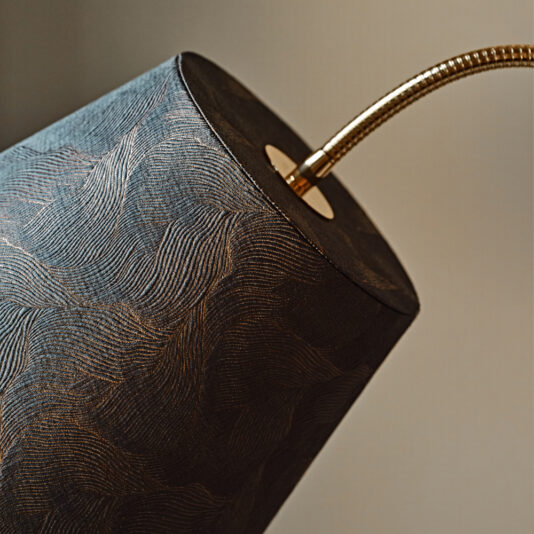 Close-up of a textured cylindrical lampshade with intricate patterns, held by a flexible, gold-colored gooseneck arm. The background is blurred and neutral, highlighting the details of this Large Modern Studio Style Floor Lamp.